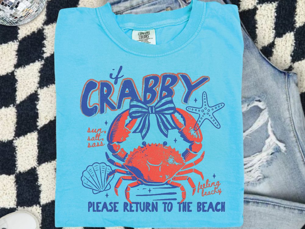 A blue t-shirt with a crab design and text, placed on a checkered surface.