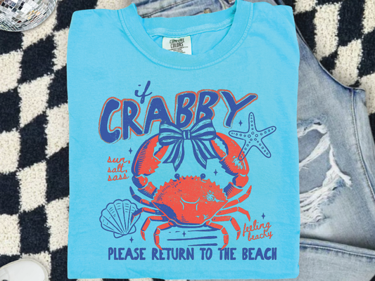 A blue t-shirt with a crab design and text, placed on a checkered surface.