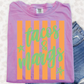 A pink t-shirt with orange and green stripes and the text "tacos & mangoes" printed on it, along with a pair of blue jeans.