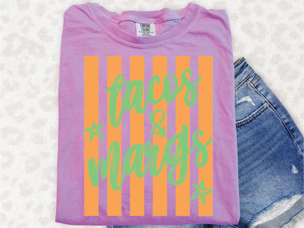 A pink t-shirt with orange and green stripes and the text "tacos & mangoes" printed on it, along with a pair of blue jeans.
