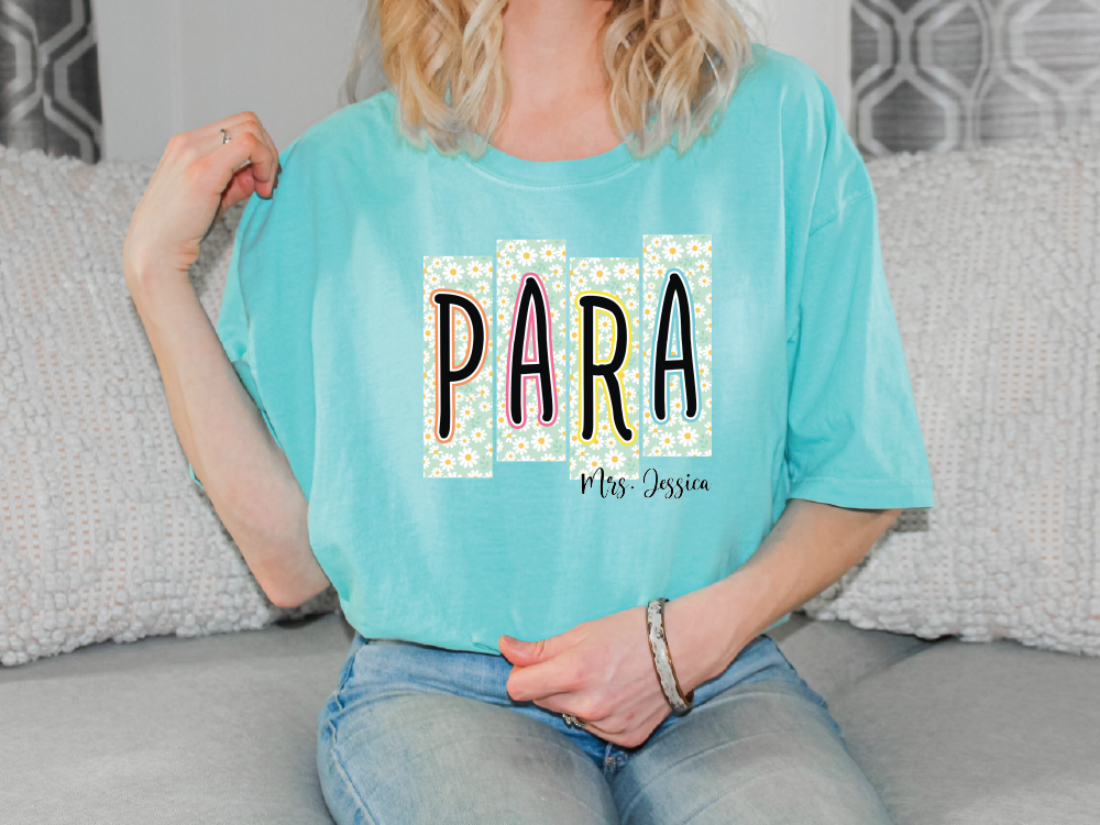 A woman wearing a turquoise t-shirt with the word "PARA" printed on it, sitting on a couch.