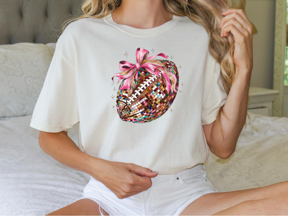 a woman sitting on a bed wearing a shirt with a football on it