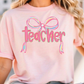 a woman wearing a pink teacher shirt with a bow