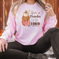 a woman sitting on the ground wearing a pink thanksgiving sweatshirt