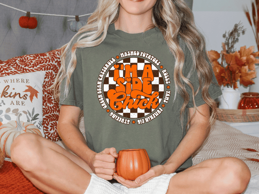 A woman wearing a green t-shirt with a graphic design is sitting on a bed, holding a pumpkin-shaped mug.