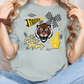 A person wearing a grey t-shirt with a tiger graphic and various text and symbols, including a checkered flag, a fan, and the word "TIGERS".