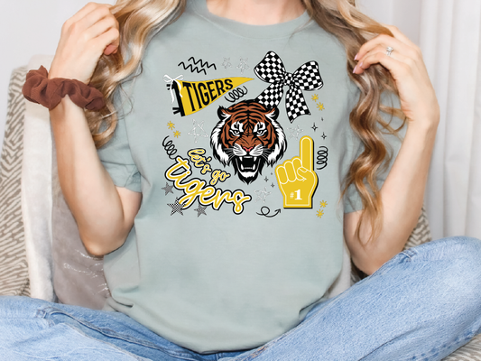 A person wearing a grey t-shirt with a tiger graphic and various text and symbols, including a checkered flag, a fan, and the word "TIGERS".