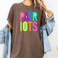 A person wearing a brown t-shirt with the text "PATRIOTS" in colorful letters, paired with a denim jacket, stands against a white background.