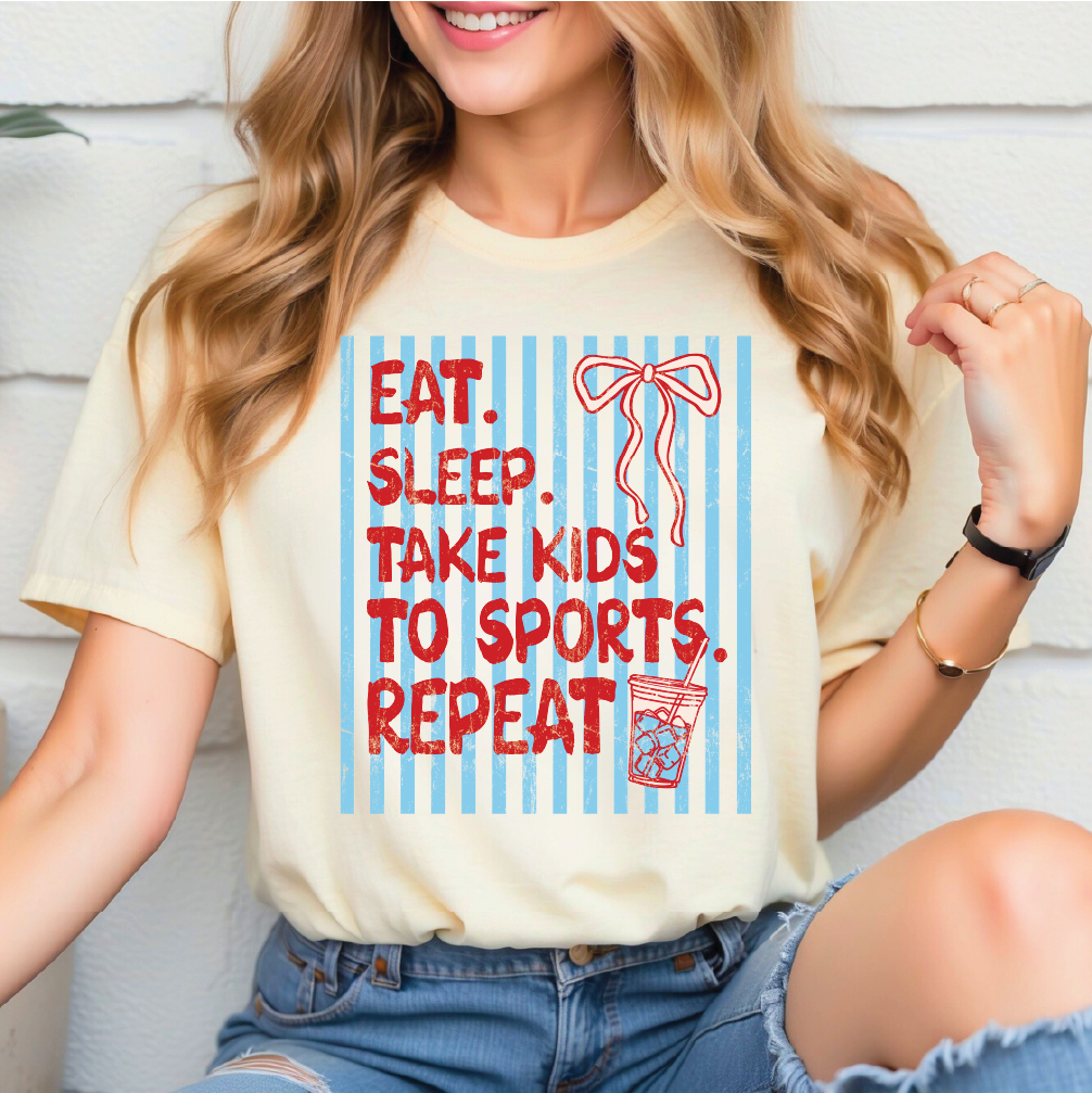 A woman wearing a yellow t-shirt with a graphic design that says "EAT. SLEEP. TAKE KIDS TO SPORTS. REPEAT" along with a bow and a drink.