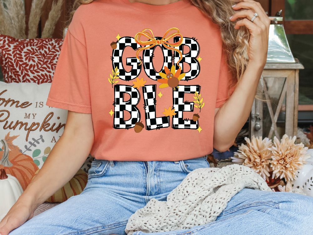 A person wearing a red t-shirt with the word "GOBBLE" printed on it, sitting on a couch with a white blanket and some fall decorations in the background.