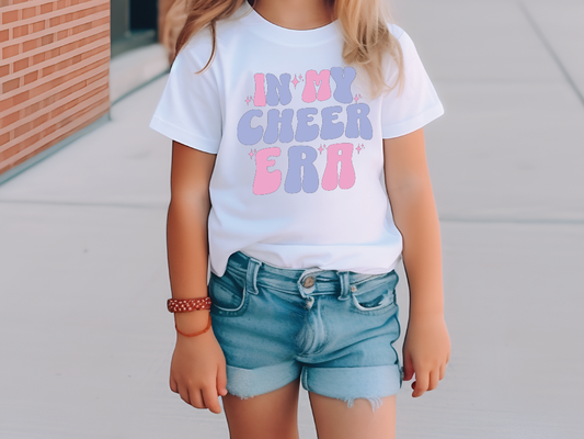 a little girl standing on a sidewalk wearing a shirt that says in my cheer era