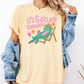 A person wearing a yellow t-shirt with a graphic of a green alligator sitting in a chair and the text "IT'S 50 CLOCK SOMEWHERE" printed on it.