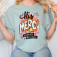 A woman wearing a light blue t-shirt with a graphic design that says "His Mercy" and "Rewrote My Story".