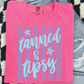 A pink t-shirt with a graphic design and text printed on it, placed on a checkered surface.