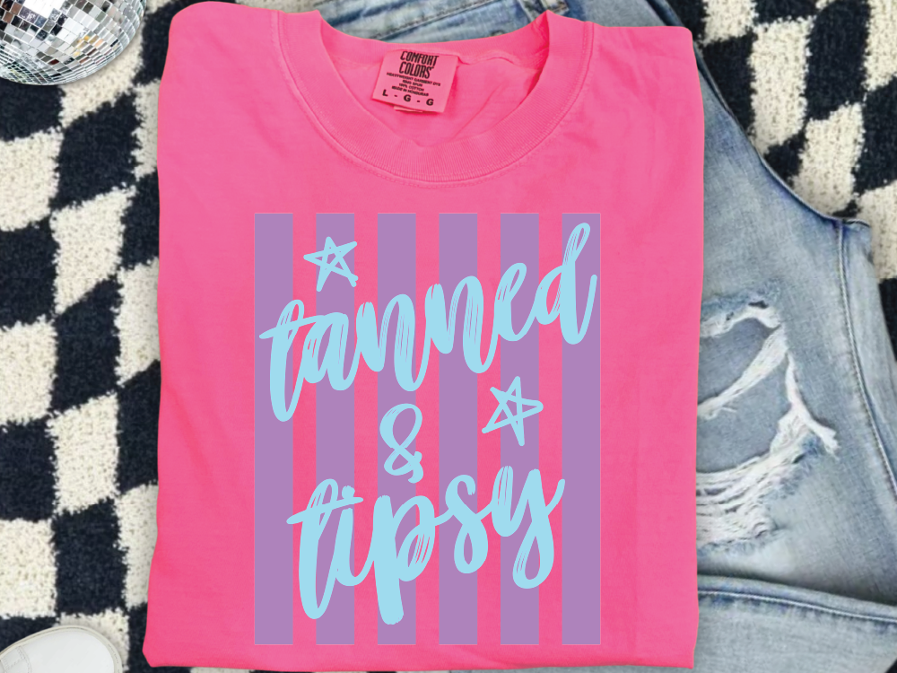 A pink t-shirt with a graphic design and text printed on it, placed on a checkered surface.