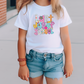 a little girl standing on a sidewalk wearing a white t - shirt