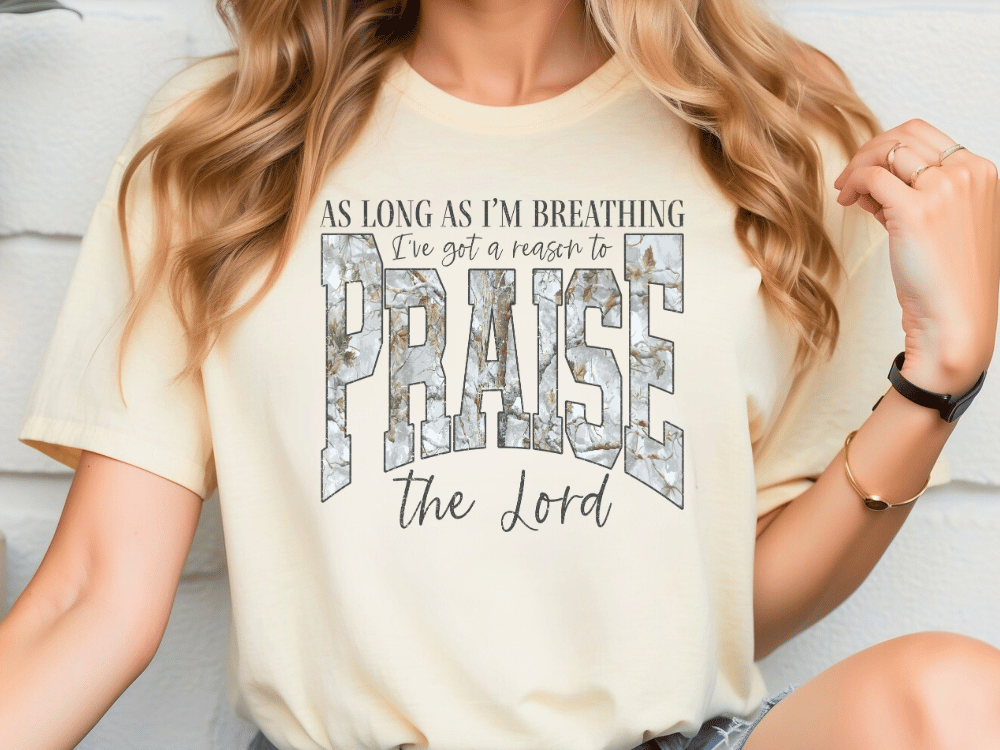 A woman wearing a white t-shirt with a text design that says "As long as I'm breathing, I've got a reason to praise the Lord".