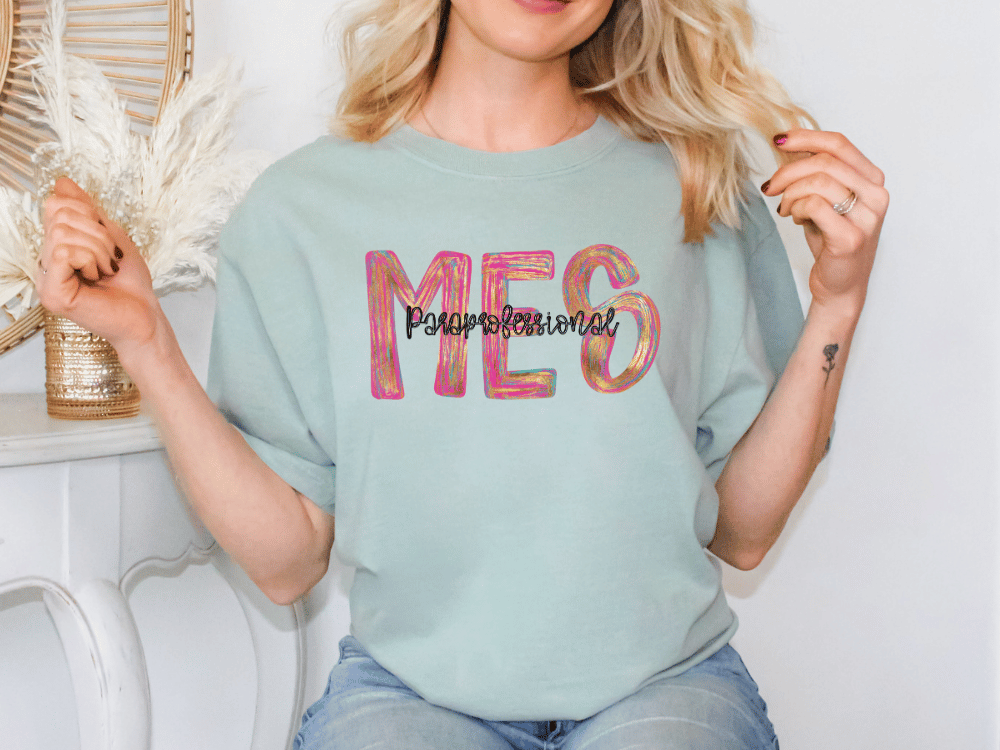 A woman wearing a light blue t-shirt with the text "MES" printed on it, posing with her hands behind her back.
