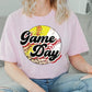 a woman sitting on a couch wearing a game day t - shirt