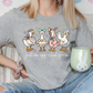 A woman wearing a gray t-shirt with a graphic of four cartoon ducks and the text "Just an egg cited goose" is sitting on a couch, holding a green mug.