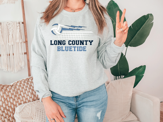 A woman wearing a gray sweatshirt with the text "LONG COUNTY BLUETIDE" printed on it, standing in front of a plant.
