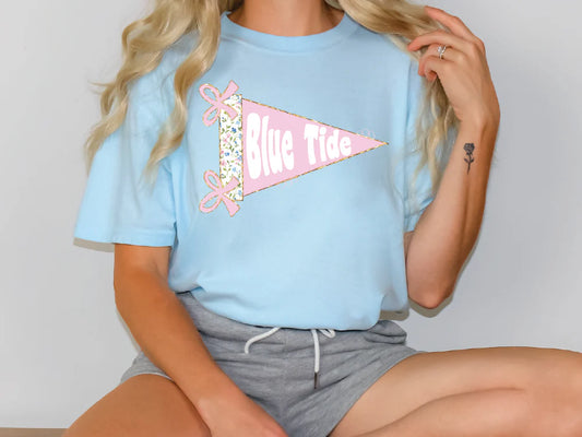 A woman wearing a light blue t-shirt with a pink and white flag design and the text "Blue Tide" on it.
