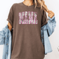 A woman wearing a brown t-shirt with the word "MAMA" printed on it, along with a denim jacket, stands against a white background.
