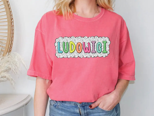 a woman standing in front of a wall wearing a pink shirt that says ludo