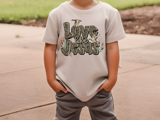 A child wearing a white t-shirt with the text "Love is like Jesus" printed on it.