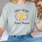 a woman sitting on a bed wearing a shirt that says first grade your name