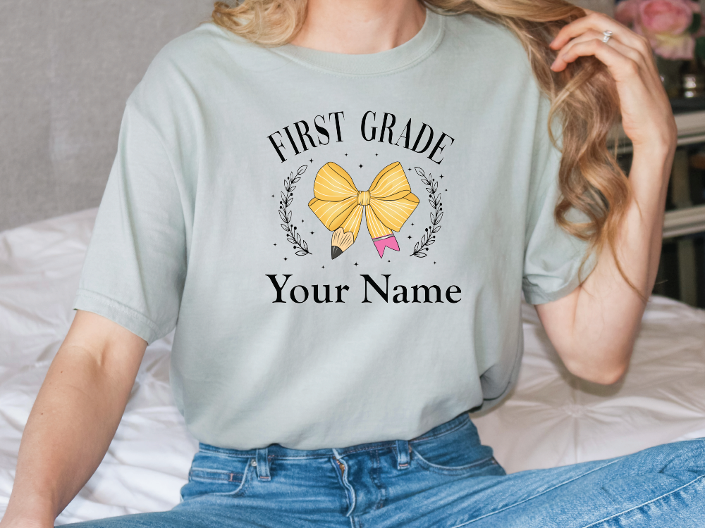 a woman sitting on a bed wearing a shirt that says first grade your name