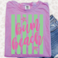 A pink t-shirt with the text "Bum Beach" printed on it, along with green and white striped patterns, is displayed alongside a pair of blue denim shorts.