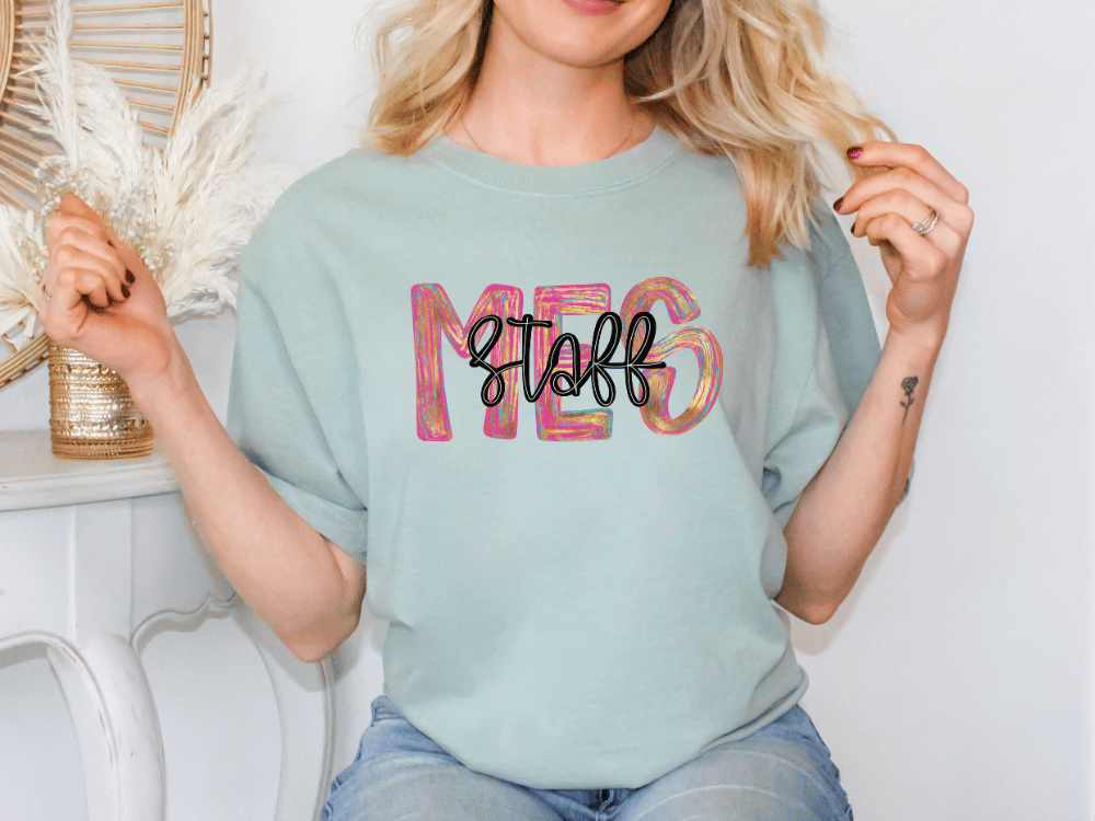 A woman wearing a light blue t-shirt with the word "STAFF" printed on it, sitting in front of a white wall with a decorative item behind her.