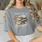 A woman wearing a gray t-shirt with a graphic design of books and flowers, along with the text "Books are my therapy".