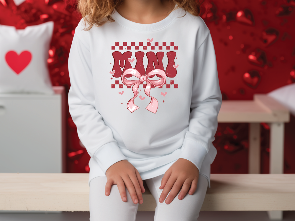 a little girl sitting on a bench wearing a sweatshirt with a pink ribbon on it