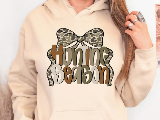 A person wearing a beige hoodie with a graphic design that says "Hunting Season" on it.