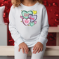 a little girl sitting on a bench wearing a sweatshirt with hearts on it