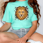 A person wearing a turquoise t-shirt with a lion graphic and gray shorts is sitting on the floor.