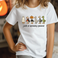 A person wearing a white t-shirt with a graphic design of five cartoon goose characters, including a ghost, a pumpkin, a skeleton, a mummy, and a green goose, along with the text "Just a spooky goose".
