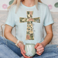 A person is sitting on a couch, wearing a light blue t-shirt with a camouflage cross design, and holding a mug with a bunny face.