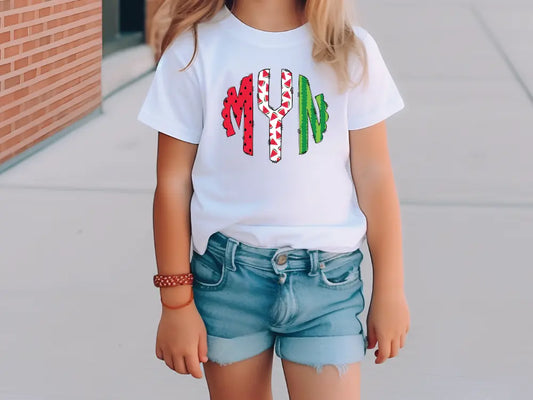 a little girl standing on a sidewalk wearing a white shirt with candy canes on