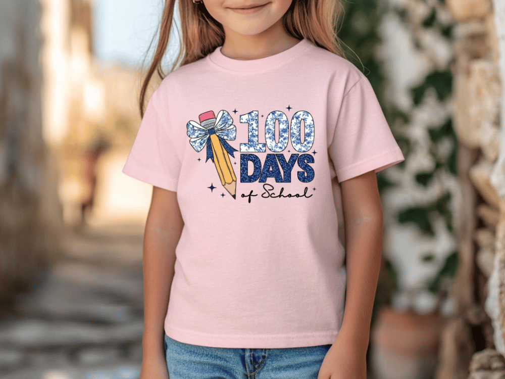 A young girl wearing a pink t-shirt with a graphic design that says "100 DAYS of School" and features a pencil and a bow.