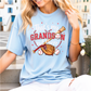 A woman wearing a light blue t-shirt with a graphic design of baseball equipment and the text "That's my GRANDson out there".