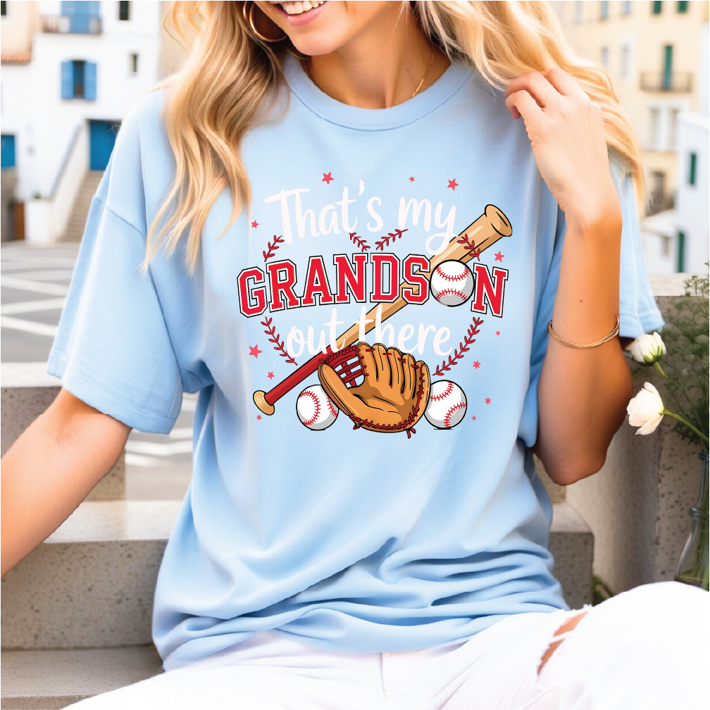 A woman wearing a light blue t-shirt with a graphic design of baseball equipment and the text "That's my GRANDson out there".