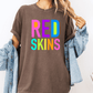 A person wearing a brown t-shirt with the text "RED SKINS" in colorful letters, along with a denim jacket, stands against a white background.