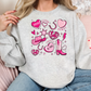 a woman sitting on a pink couch wearing a grey sweatshirt with pink hearts and a