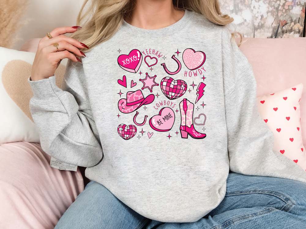 a woman sitting on a pink couch wearing a grey sweatshirt with pink hearts and a