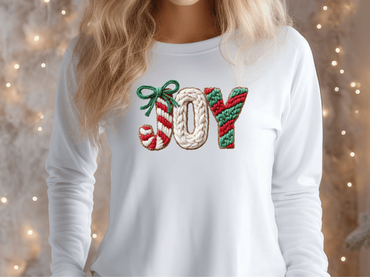 A woman wearing a white long-sleeved shirt with the word "Joy" embroidered on it.