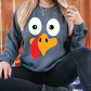 a woman sitting on the ground wearing a sweatshirt with a turkey face on it