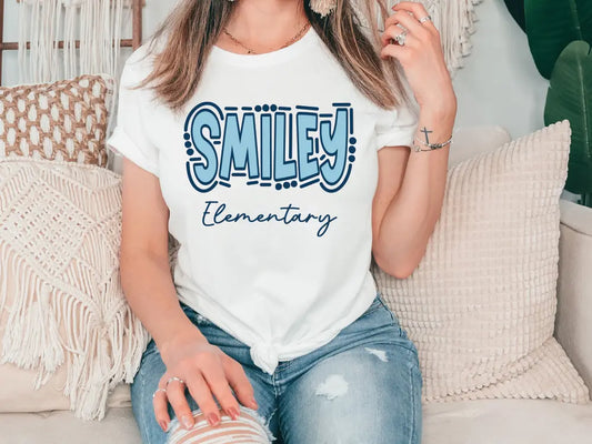 a woman sitting on a couch wearing a smile elementary shirt